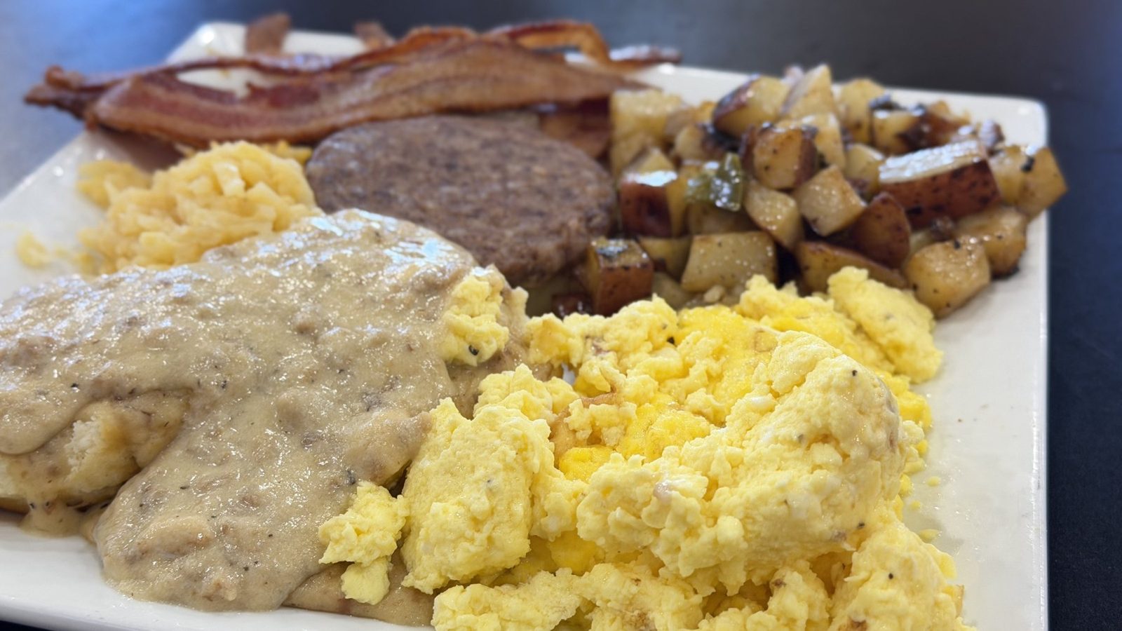 Breakfast plate with biscuits and gravy, scrambled eggs, sausage, bacon and home fries