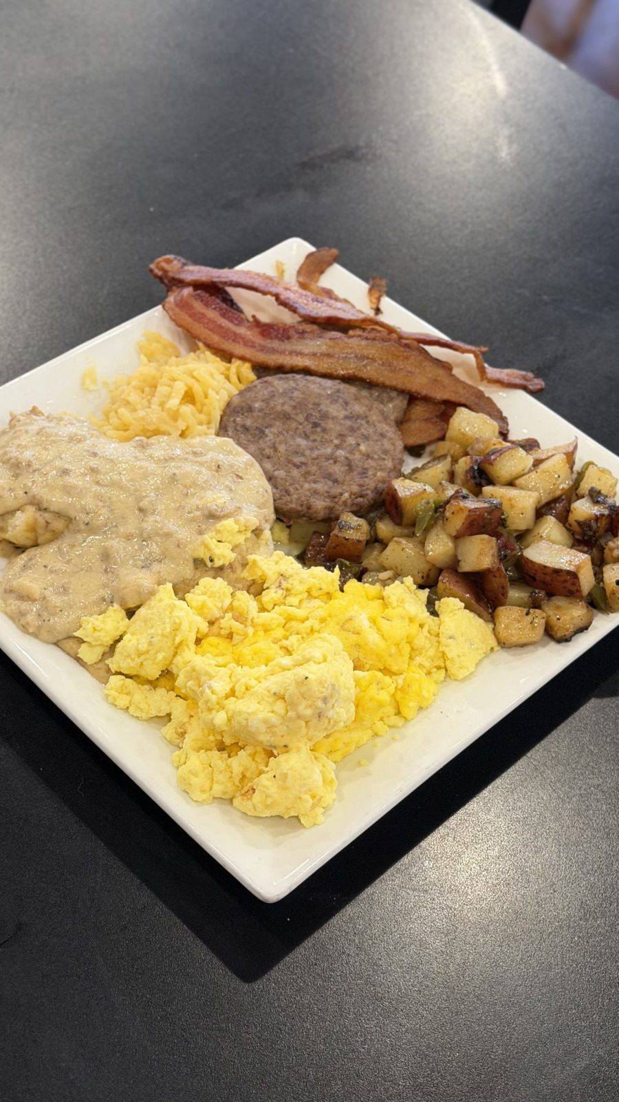 Breakfast plate with bacon, sausage, eggs, biscuits and gravy and home fries